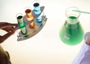 Unrecognizable ethnic scientist in white coat putting tube into flask with liquid substance while conducting chemical experiment with reagents in test tubes in laboratory